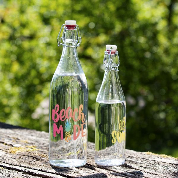 Two glass bottles of different sizes are printed in multiple colours and stand on a piece of bark covered with a little moss. 